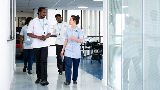Two nursing students in uniform walk down a corridor whilst in discussion with one another